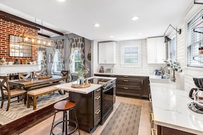 A modern kitchen with a brick accent wall, white cabinetry, and a central island with seating.