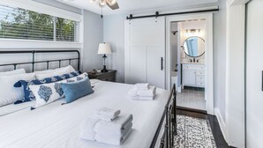 A bedroom with a bed, bedside table, lamp, and a view of the bathroom. - Southern Charm w/ High-end Modern Amenities + Parking by Lucky Savannah (Savannah)