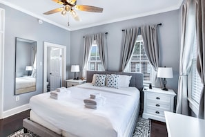 A modern hotel room with a large bed, two bedside tables, a ceiling fan, and a view of the outdoors.