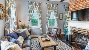 A living room with a fireplace, leather sofa, patterned rug, and large windows with curtains. - Southern Charm w/ High-end Modern Amenities + Parking by Lucky Savannah (Savannah)