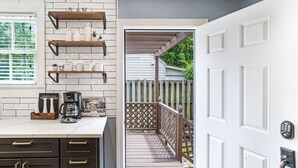 A kitchen with dark cabinets, white countertops, and a coffee maker. There is a wooden deck leading to a white door with a keypad lock. - Southern Charm w/ High-end Modern Amenities + Parking by Lucky Savannah (Savannah)