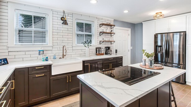 A modern kitchen with dark cabinetry, white countertops, a central island with an induction cooktop, and stainless steel appliances. - Southern Charm w/ High-end Modern Amenities + Parking by Lucky Savannah (Savannah)