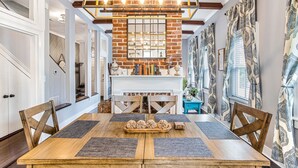 A dining area with a wooden table, chairs, and a brick wall with a mirror. - Southern Charm w/ High-end Modern Amenities + Parking by Lucky Savannah (Savannah)