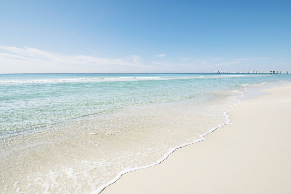 Uma praia com águas cristalinas e um cais ao longe.