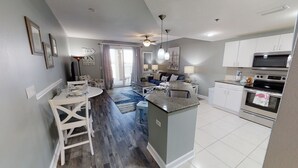 A modern kitchen with white cabinets, a central island, and a dining area with a white table and chairs. - Renovated with Gulf View Free Beach Chairs, Golf, & Activities Daily! (Panama City Beach)