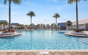 Uma grande piscina ao ar livre com palmeiras e espreguiçadeiras, rodeada por edifícios de um resort.