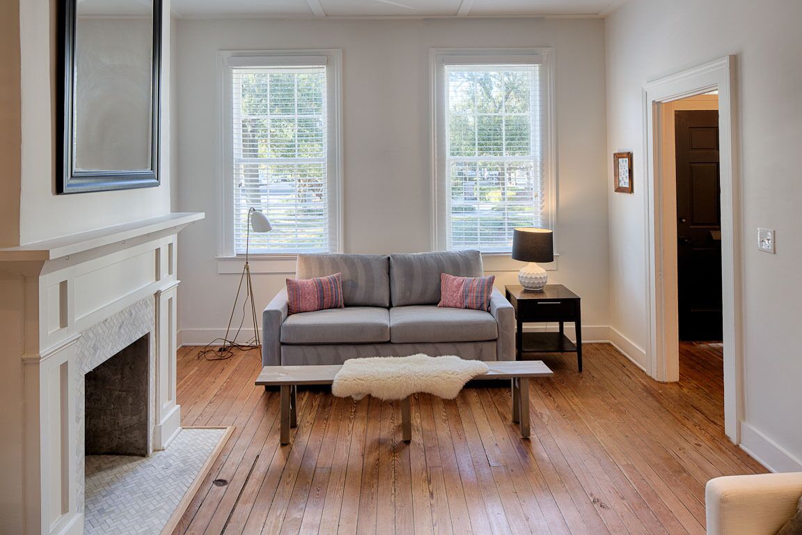 A living room with a fireplace, a gray sofa with colorful pillows, a white fur throw, and a small table with a lamp.