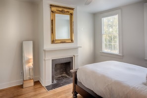 A bedroom with a fireplace, a bed, a mirror, and a window.