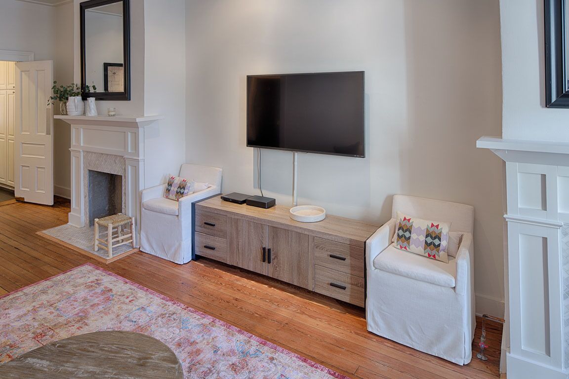 Un salon moderne avec une cheminée, un téléviseur fixé au mur et deux fauteuils blancs.