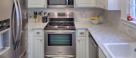 Een moderne keuken met roestvrijstalen apparatuur, witte keukenkastjes en een marmeren aanrecht.