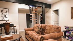 A living room with a brown leather sofa, a wooden coffee table, a spiral staircase, and a bookshelf.