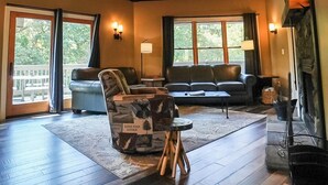 A spacious living room with a high ceiling, wooden beams, a large window, and a cozy seating area with a sofa and armchairs.