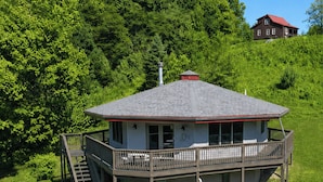 A two-story building with a balcony and a staircase, surrounded by lush greenery.