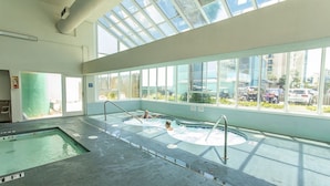An indoor swimming pool with clear glass walls, a separate hot tub area, and a view of the cityscape through large windows. - ONE BEDROOM CONDO TO DIE FOR  Royal Garden 803 (Murrells Inlet)