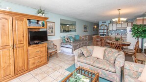 A spacious living room with a large wooden cabinet, a television, a sofa, and a dining area with a chandelier. - ONE BEDROOM CONDO TO DIE FOR  Royal Garden 803 (Murrells Inlet)