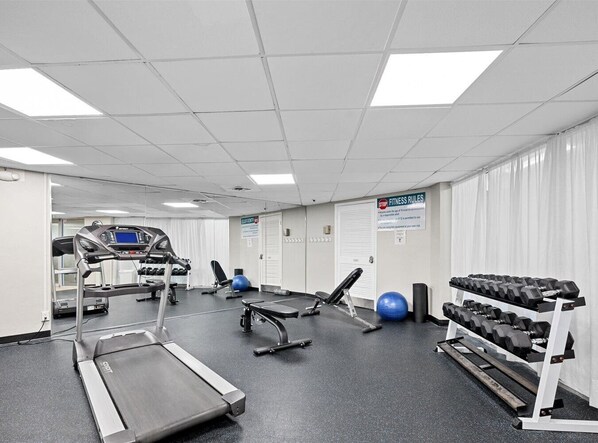Een sportschool met loopbanden, gewichten, fitnessballen en een bank.
