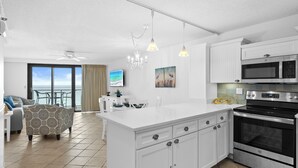 A modern kitchen with white cabinetry, a large island, stainless steel appliances, and a view to the outside. - Rate Reduced! Beachfront 2BR w/ Gulf Views, GOLF CART! Steps to Beach & Pool. (Destin)