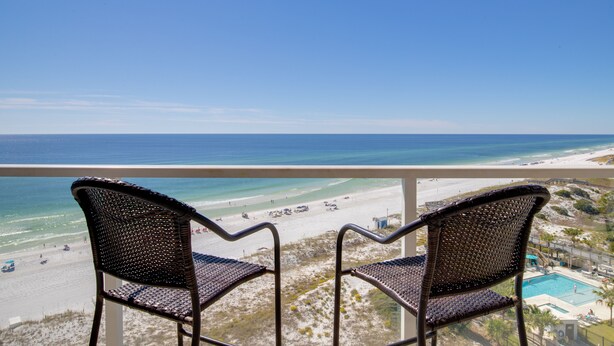 A balcony with two wicker chairs overlooking a beach and a pool. - Rate Reduced! Beachfront 2BR w/ Gulf Views, GOLF CART! Steps to Beach & Pool. (Destin)