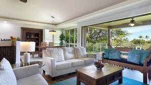 Un salón espacioso con sofá, sillones, una mesa de centro y una zona de comedor con mesa y sillas. Un ventanal grande ofrece vistas al exterior.