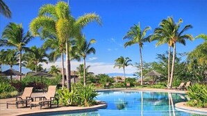 Un área de piscina con sillones de descanso y palmeras.