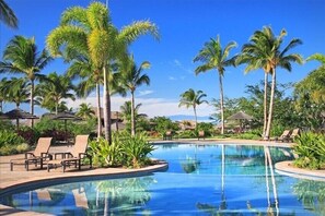 Relax by the serene pool surrounded by lush palm trees and lounge chairs.