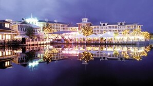 Ein Hotel am Wasserufer mit mehreren Gebäuden, Außenbereichen zum Sitzen und einem Spiegelbild im Wasser.
