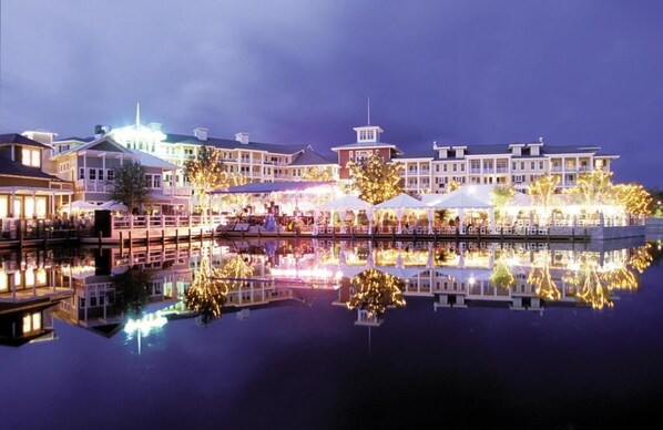 A waterfront hotel with multiple buildings, outdoor seating areas, and a reflection in the water.