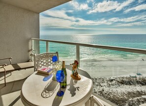 A balcony with a table set for two, overlooking a beach.