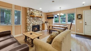 A living room with a stone fireplace, wooden furniture, and large windows.