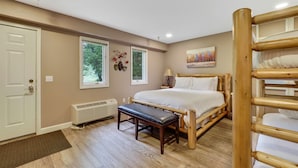A bedroom with a bed, bench, bedside table, lamp, and a painting on the wall.