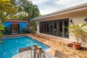 A swimming pool with a tiled deck, a wooden deck chair, and a small outdoor seating area. - Casa Serena in Key Biscayne (Key Biscayne)