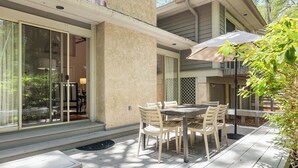 An outdoor patio with a table and chairs, a covered area with an umbrella, and a sliding glass door leading to an interior space.