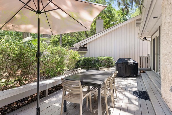 Un patio al aire libre con una mesa y sillas, una parrilla cubierta y una terraza de madera.