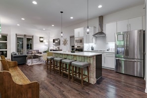 A modern kitchen with stainless steel appliances, a bar area with stools, and a dining area with a sofa and chairs. - The New Nashview: 4BR Gulch | Rooftop Fire Pit (Nashville)