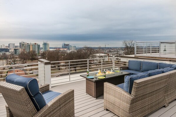 A rooftop deck with wicker furniture, a fire feature, and a city view.