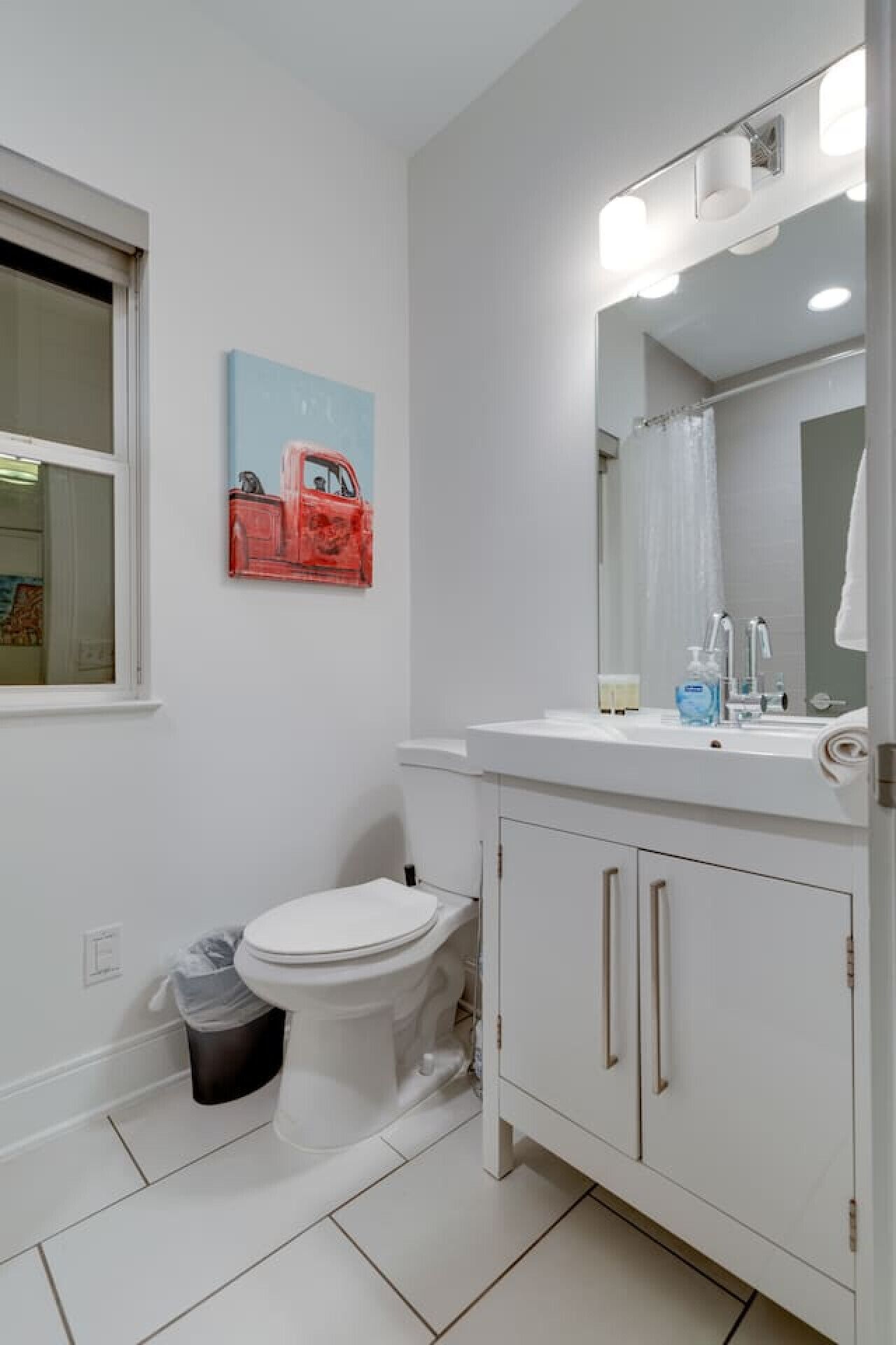 Une salle de bain avec des toilettes blanches, un lavabo avec un miroir et une poubelle.