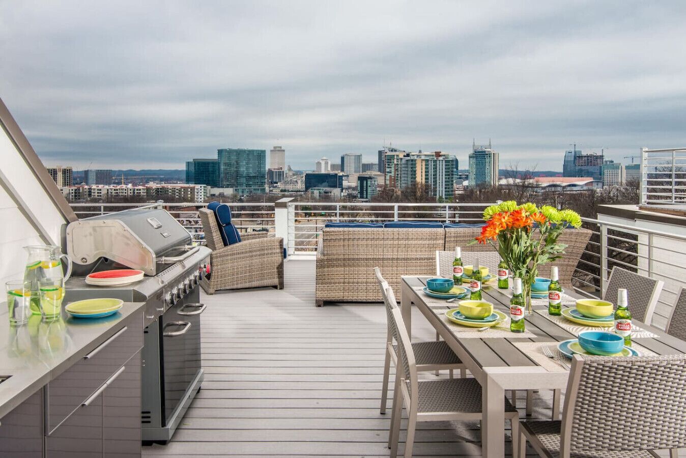 Une terrasse sur le toit, dotée d'un barbecue, de meubles en osier et d'une table dressée pour les repas, offrant une vue panoramique sur la ville.