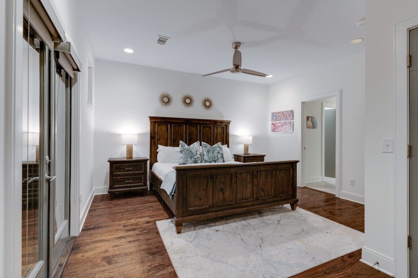 Une chambre à coucher avec un grand lit en bois, deux tables de chevet avec des lampes, un ventilateur de plafond et un tapis en marbre blanc.