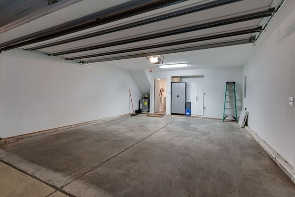 A spacious, unfinished interior with concrete floors and white walls, featuring a door, a ladder, and some construction materials.