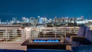 Eine Dachterrasse mit Feuerstelle, Sitzgelegenheiten im Freien und Blick auf die Stadtlandschaft.
