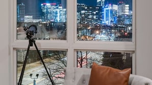 Ein Zimmer mit großem Fenster und Blick auf die nächtliche Stadtlandschaft.