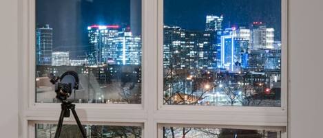 A room with a large window offering a cityscape view at night.