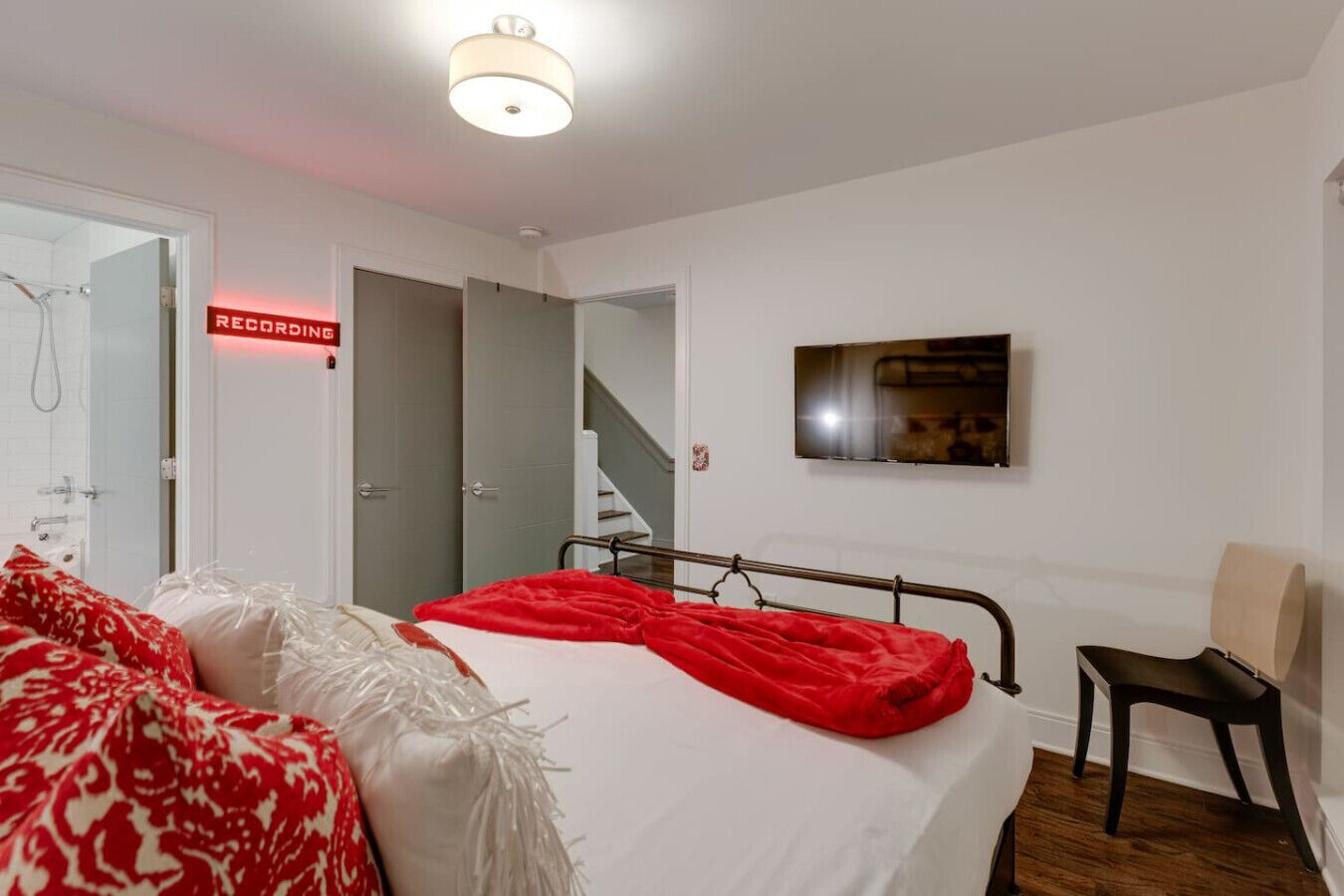 A bedroom with a bed, a chair, a TV, and a recording sign.