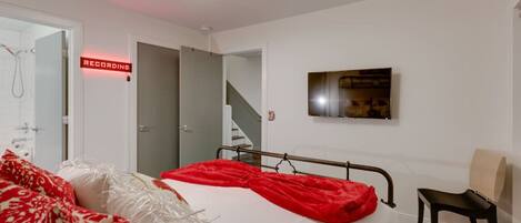 A bedroom with a bed, a chair, a TV, and a recording sign.