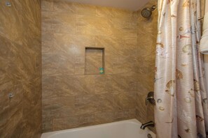 Une salle de bain avec une baignoire, une douche et une petite étagère.