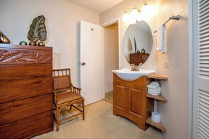A bathroom with a wooden vanity, a chair, a large mirror, and a wall-mounted light fixture. - Maui Sunset #A-117 Oceanfront Complex, Ocean View, Ground Floor, Full A/C (Kihei)