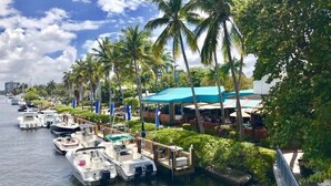 Un puerto deportivo con barcos amarrados, palmeras y un restaurante con toldo azul.