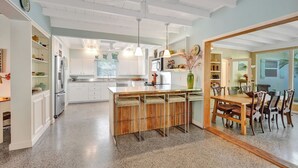 Una cocina amplia con una isla central, armarios blancos y una zona de comedor con mobiliario de madera.