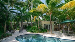 Una piscina rodeada de palmeras y un patio con mobiliario exterior.