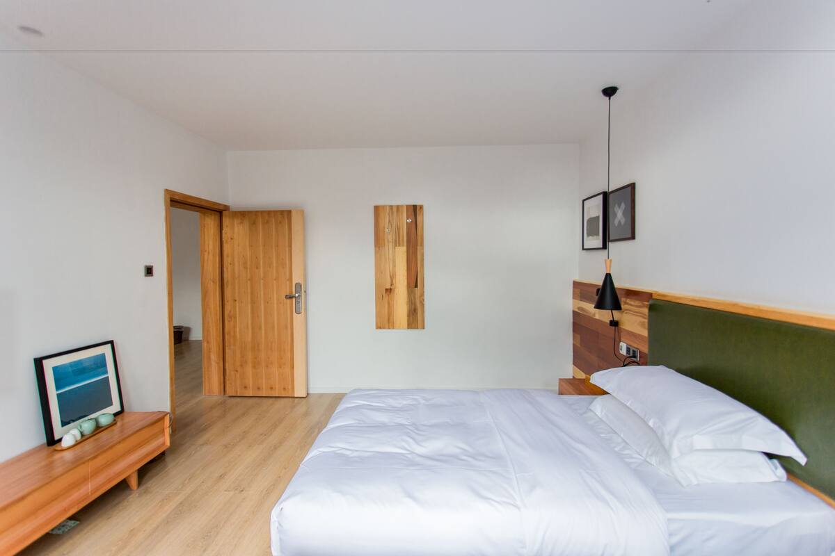 Un dormitorio con cama, una puerta de madera, un marco de cuadro y una mesita.